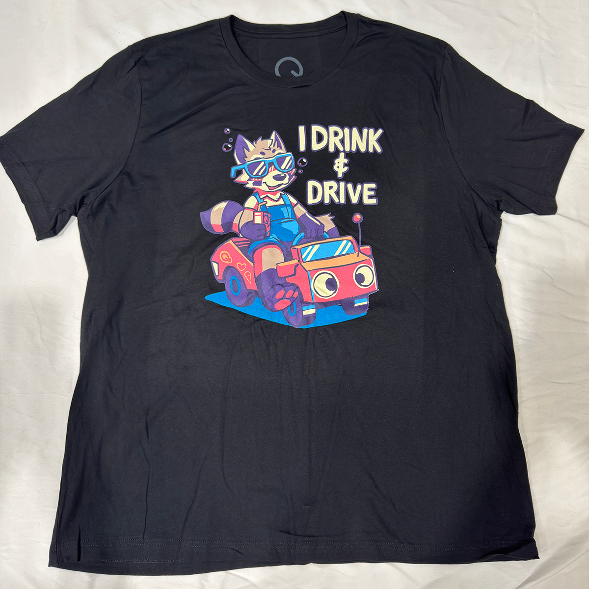 Black screen printed t-shirt with a raccoon in sunglasses; driving a toy car with the text, "I drink & drive."